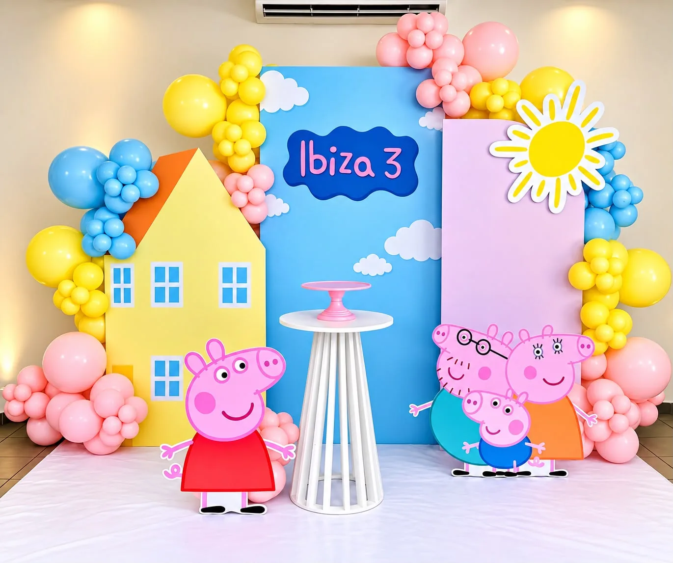 Decoración de cumpleaños de 3 años: casita amarilla troquelada, panel de cielo con nubes y nombre, sol troquelado, figuras de personajes animados y globos amarillos, rosa y azul.