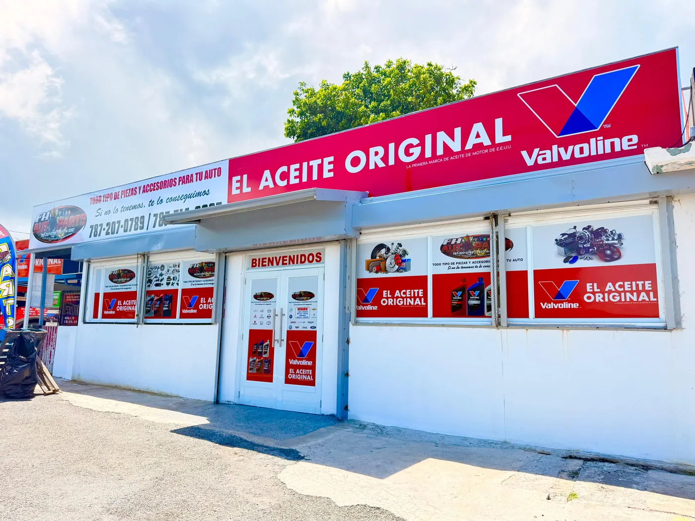 Rótulo comercial instalado en la fachada de una tienda de piezas de auto, con letras blancas sobre fondo rojo y vinilos impresos en las vitrinas.