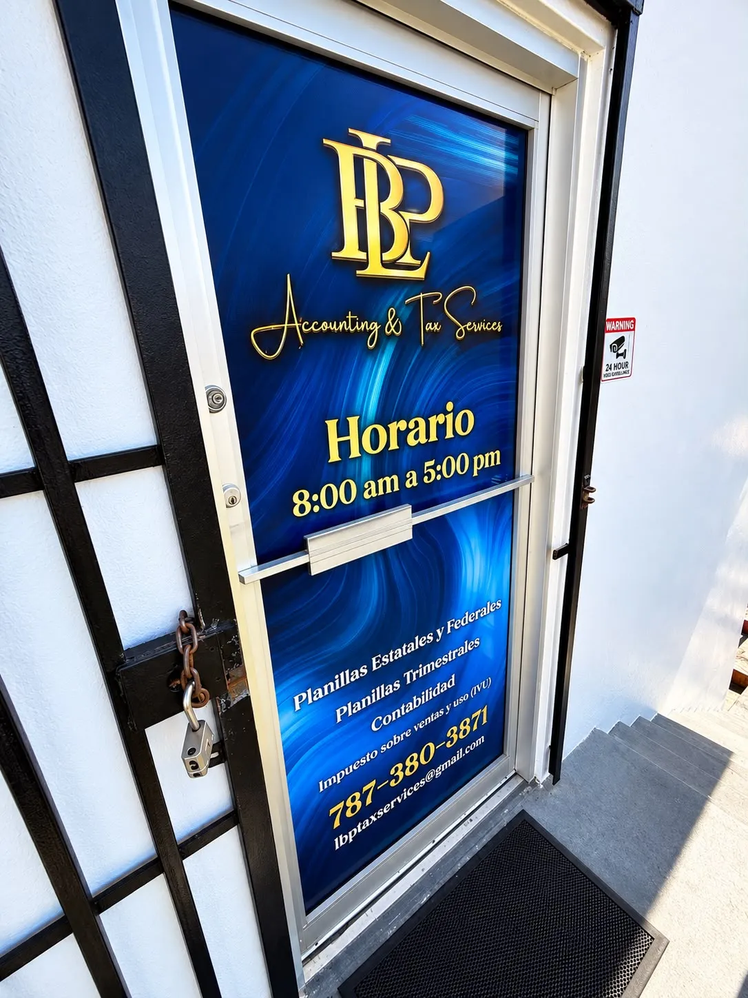 Puerta de cristal de una oficina rotulada con vinil impreso en azul y dorado, con el logo, el nombre del negocio y el horario.